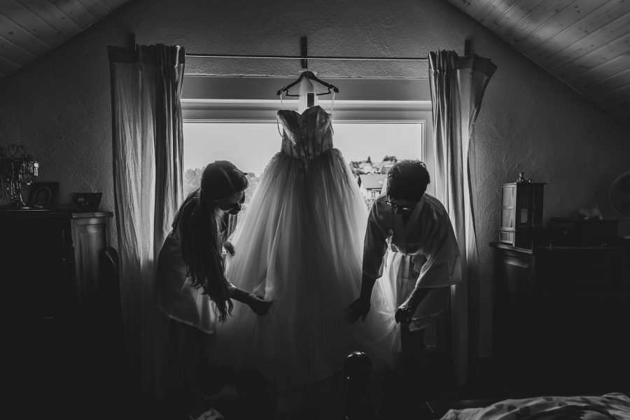 Brautkleid hängt am Fenster, zwei Frauen davor, in Schwarzweiß