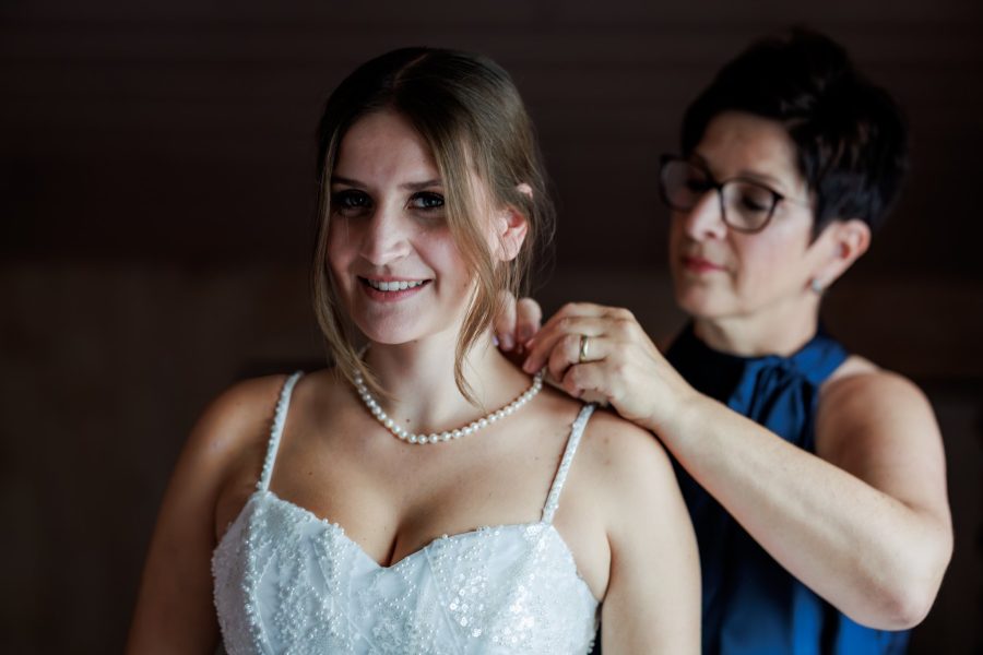 Eine Frau legt der Braut die Perlenkette an
