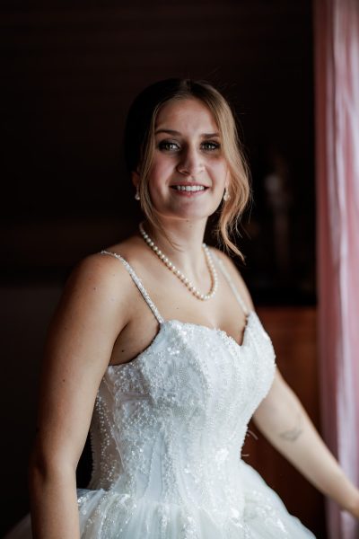 Braut im Brautkleid lächelt am Fenster