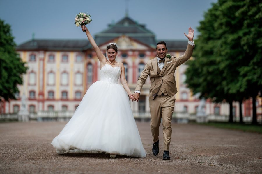 Schlosspark Bruchsal Brautpaar jubelt Hand in Hand vor Schloss Bruchsal – Schlosspark Bruchsal