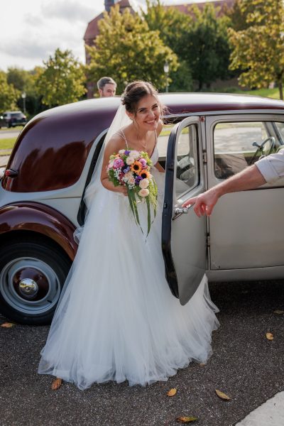 Die Braut steigt mit dem Brautstrauß aus dem Oldtimer