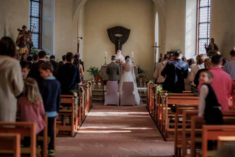 Trauung: Das Brautpaar steht vor dem Altar, die Gäste in den Bänken